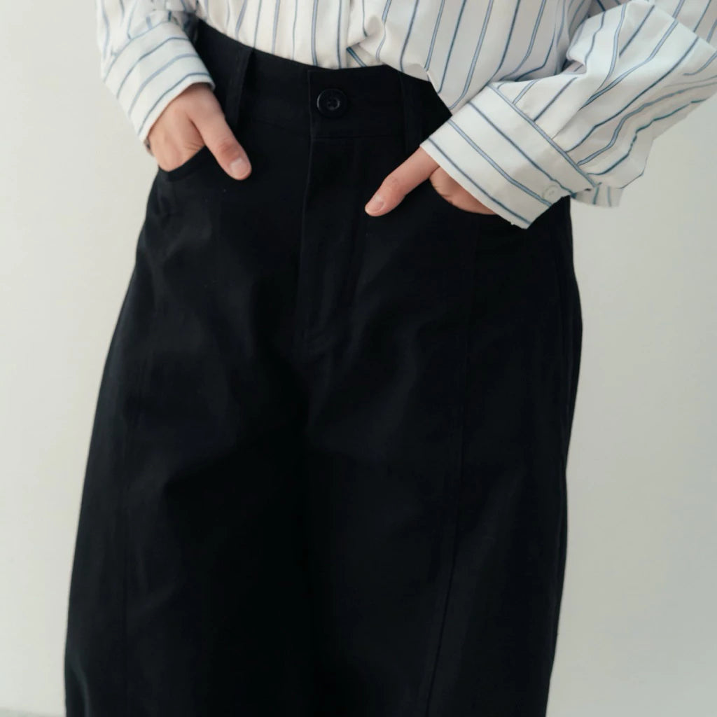 Person wearing a black wide-leg pants by notyourcompany and striped shirt against a white background