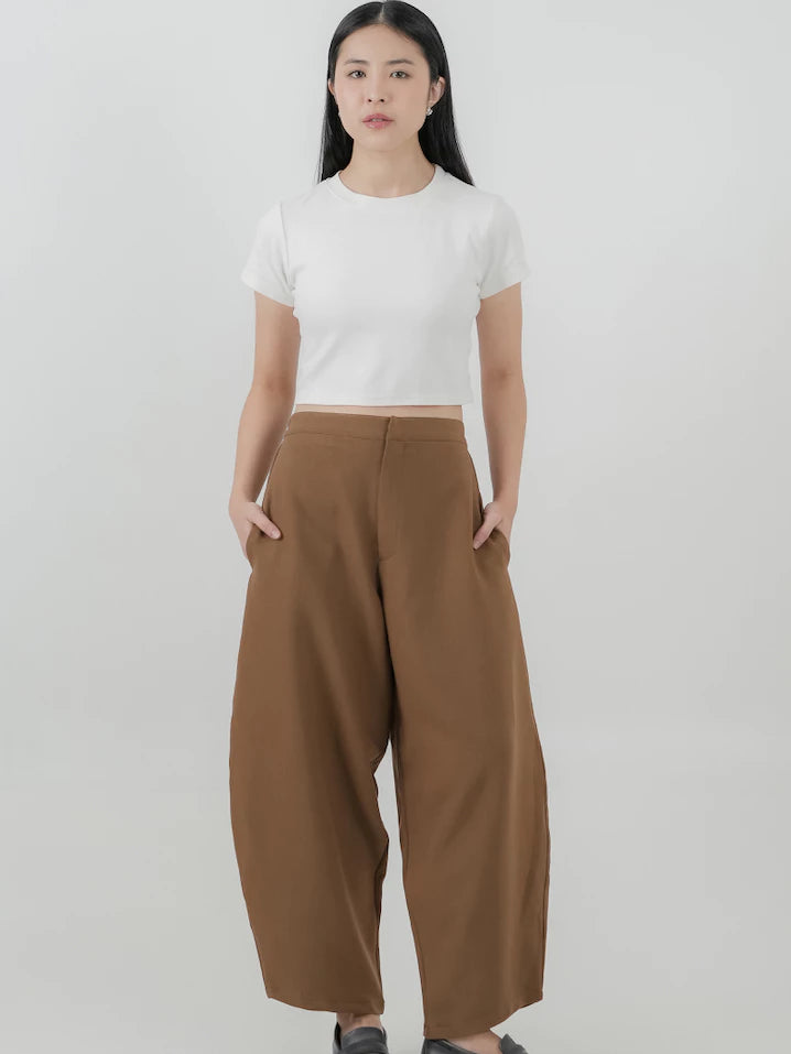 Woman wearing a white crop top and brown barrel pants on a plain background