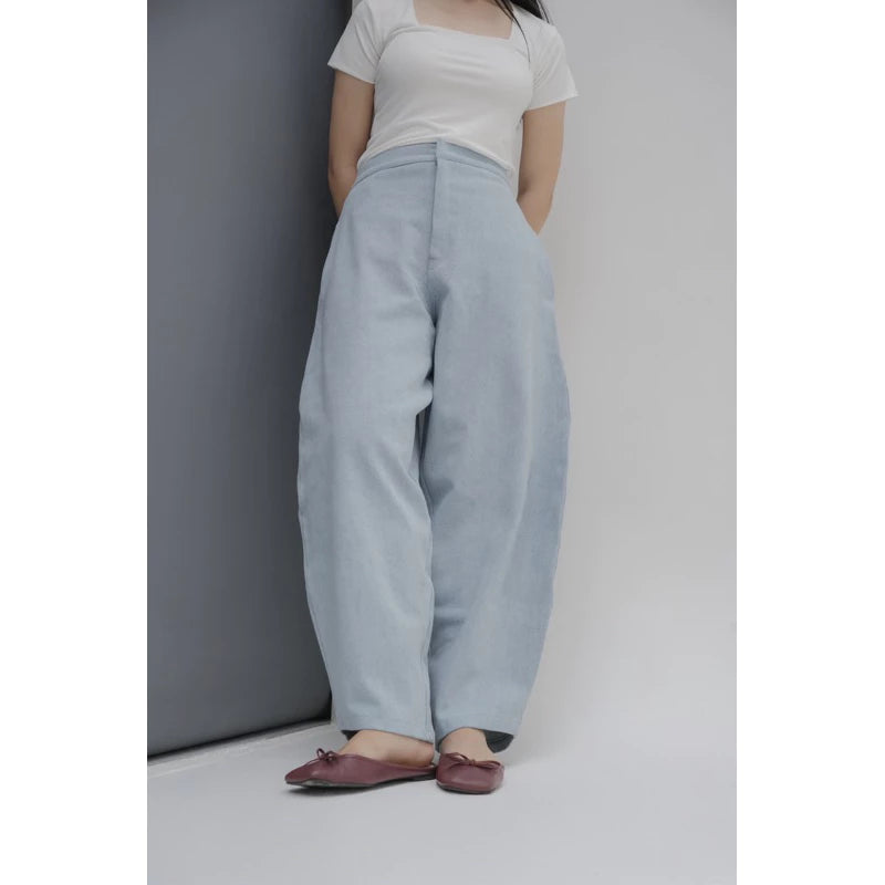 Person wearing light blue barrel pants and a white top against a neutral background