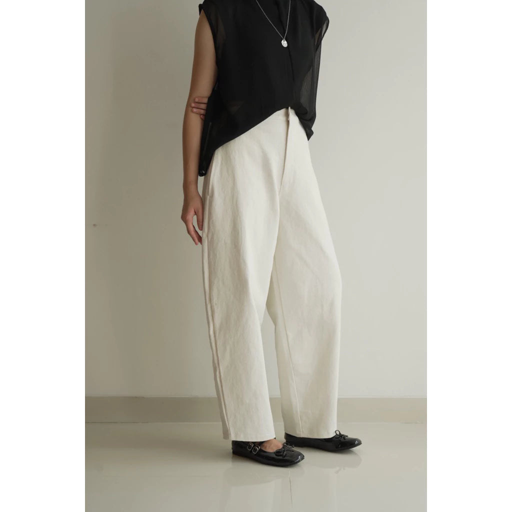 Person wearing a black top and white barrel pants on a plain background