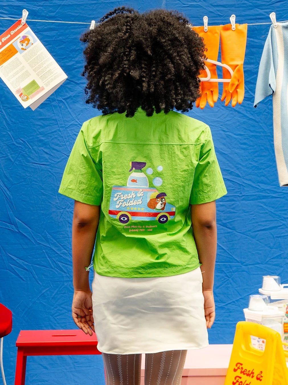 Person wearing a green workshirt by Oh.Irv with a cartoon character and text at the back.