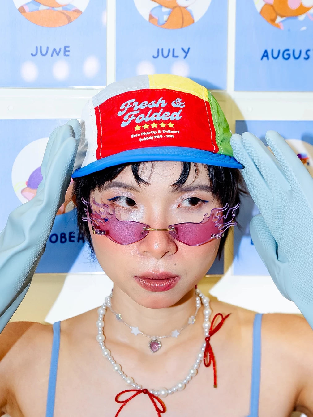 Person wearing a colorful cap by Oh.Irv and gloves with a blue background featuring months of the year.