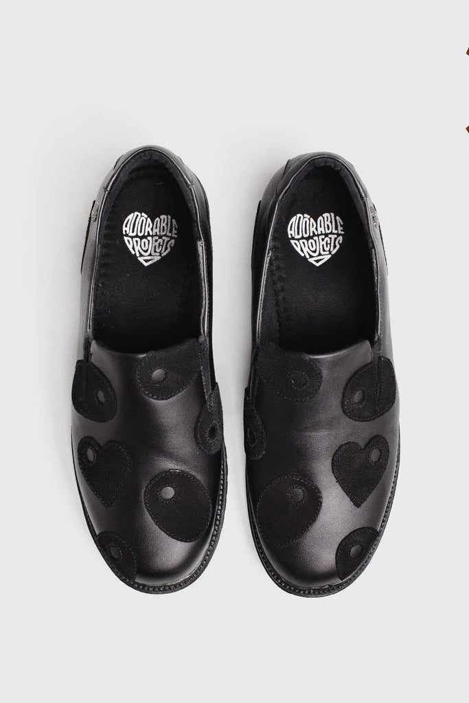 Black loafer shoes by Adorable Projects with heart patterns on a white background