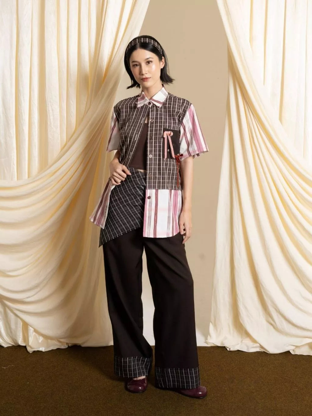 Person wearing a patterned outfit with a striped shirt by LR Studio and black pants against a draped curtain background