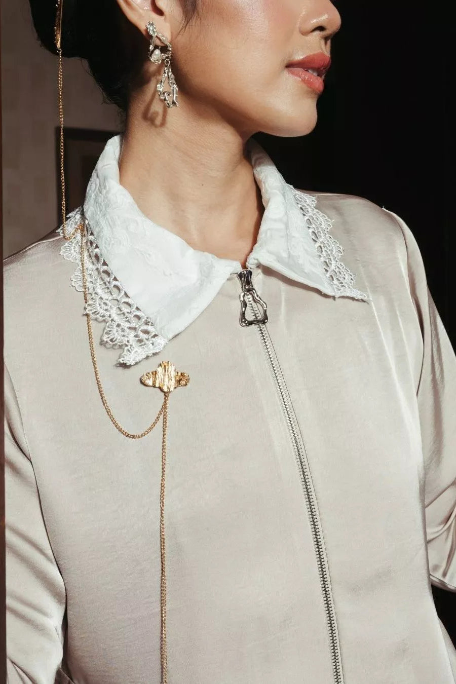 Close-up of a person wearing a beige top with a white lace collar by LR Studio and gold jewelry.
