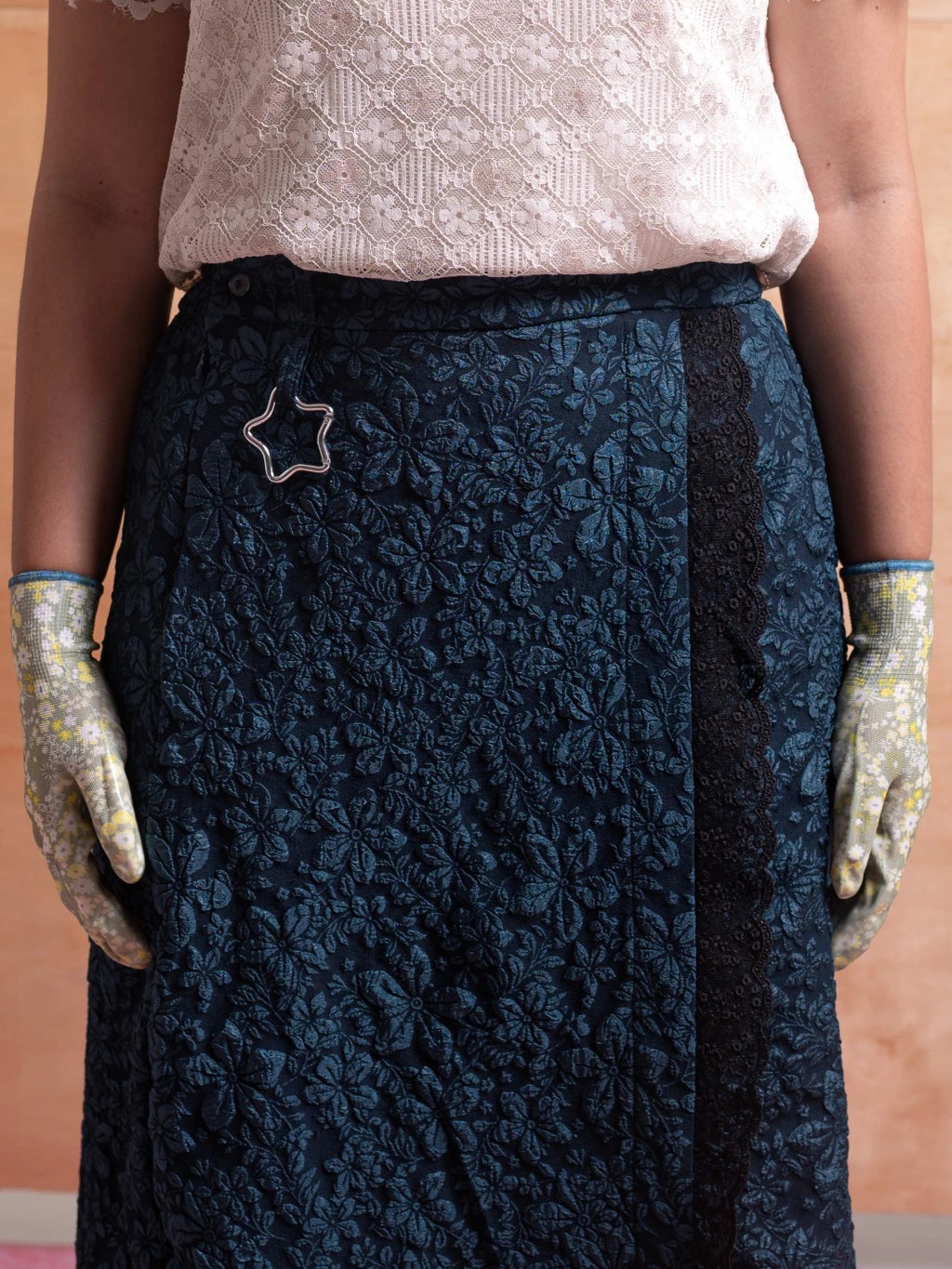 Person wearing a dark blue floral patterned skirt with a star-shaped brooch from Hintuturo.