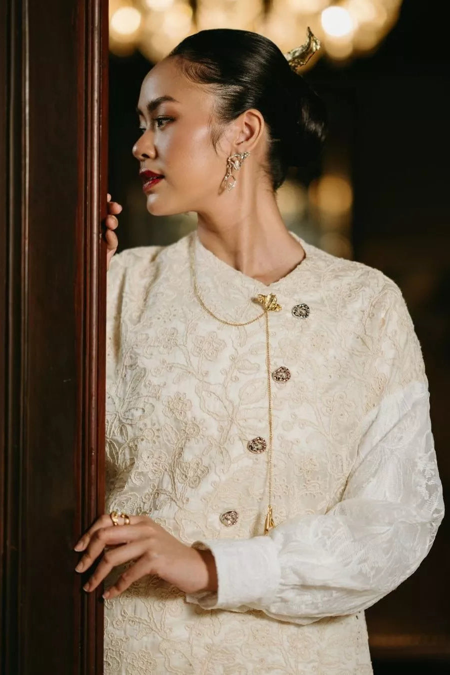 Woman wearing a detailed beige outfit with gold buttons by LR Studio in a softly blurred indoor setting