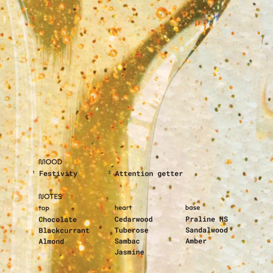 Close-up image of golden perfume liquid with shimmering particles, representing Got My Mojo Back by Alchemist Fragrance. The scent evokes a mood of “Festivity” and “Attention Getter”, featuring top notes of chocolate, blackcurrant, and almond; heart notes of cedarwood, tuberose, sambac, and jasmine; and base notes of praline HS, sandalwood, and amber—a rich gourmand woody composition.