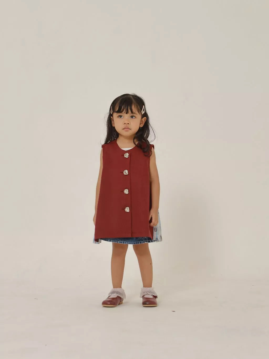 Young girl wearing a red sleeveless vest with buttons on a plain background