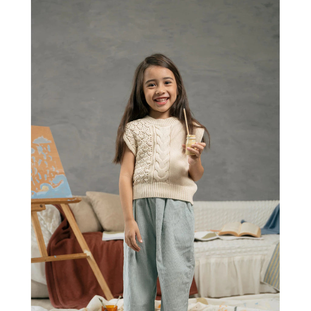 Young girl holding a glass of juice in a cozy living room setting wearing knitted Gipsy Vest from Sabine & Heem