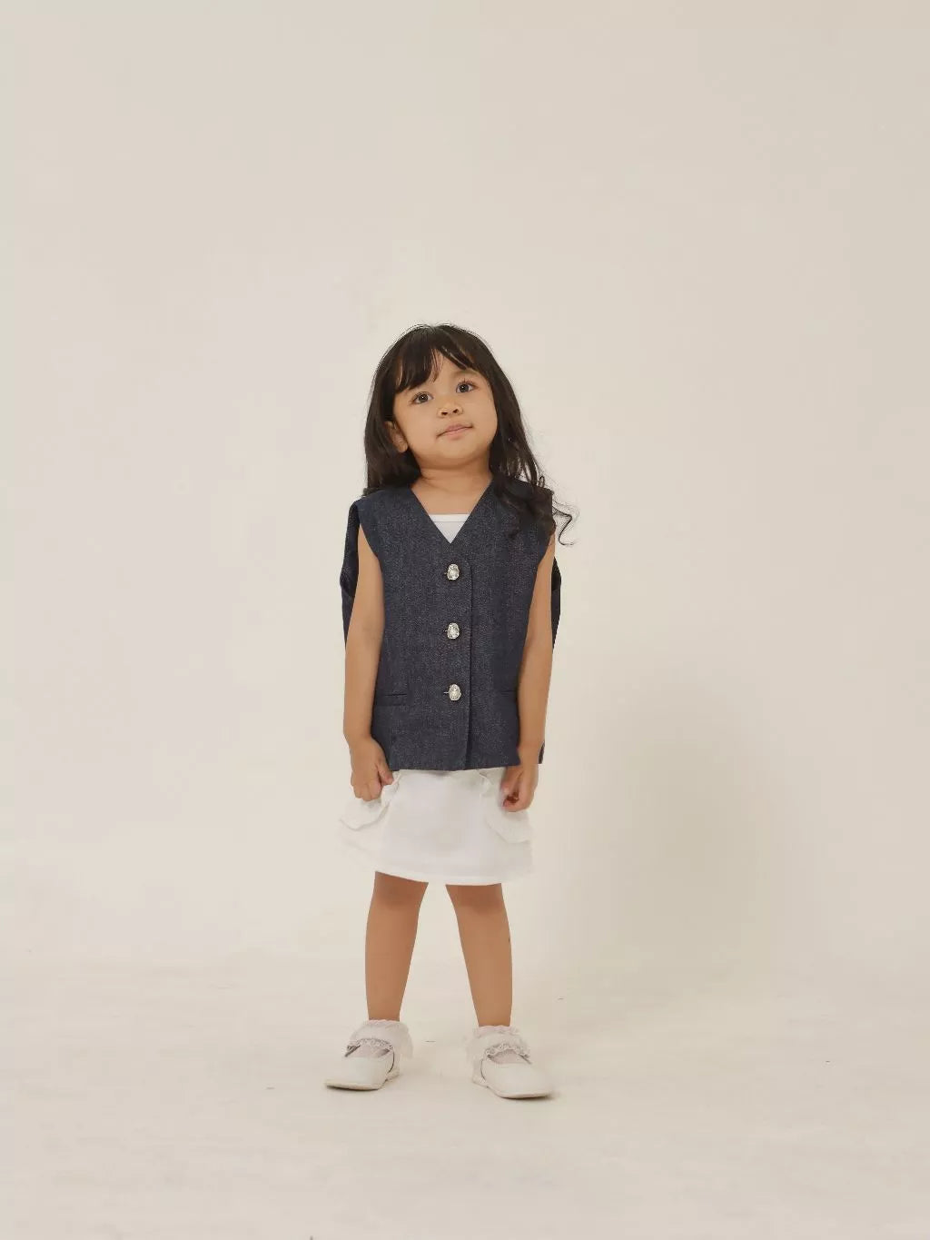 Child wearing a denim vest and white shorts on a plain background