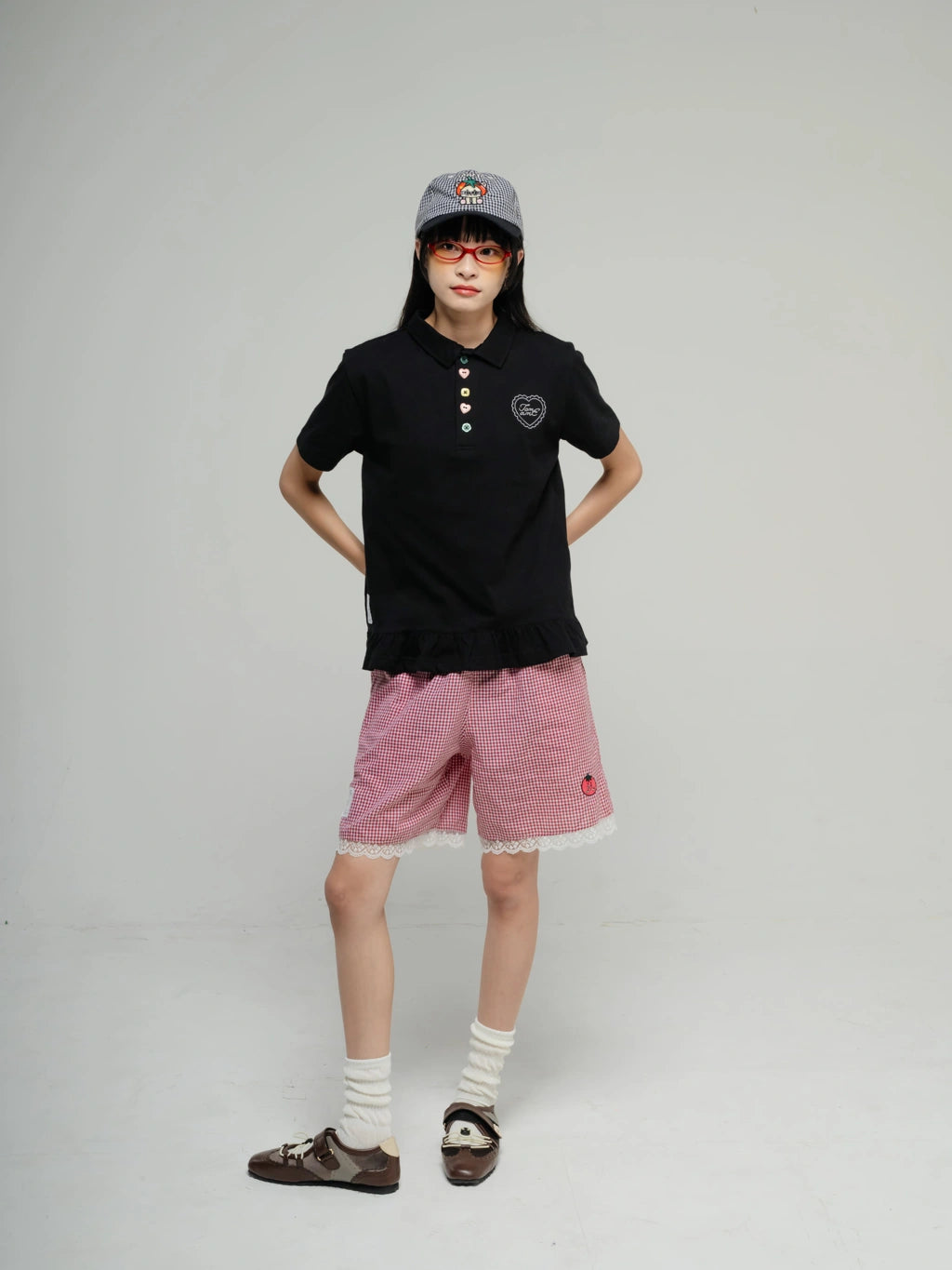 Person wearing a black polo shirt by Tome Ame, pink shorts, and a gray cap on a plain background