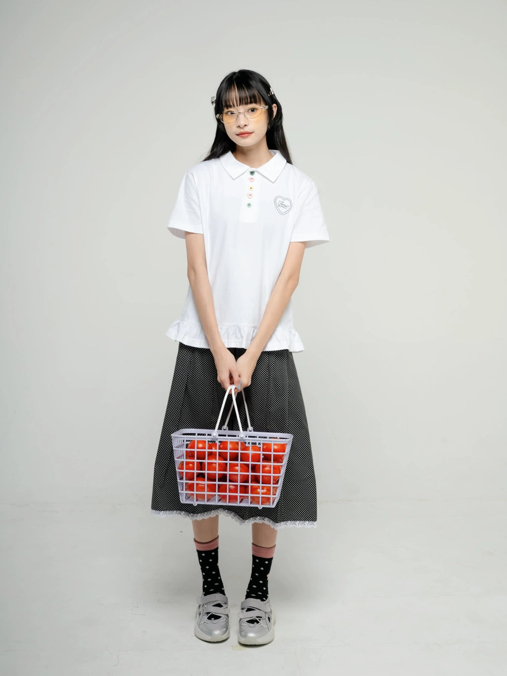 Person wearing a white polo shirt by Tome Ame and black skirt holding a transparent bag with red and blue pattern on a plain background