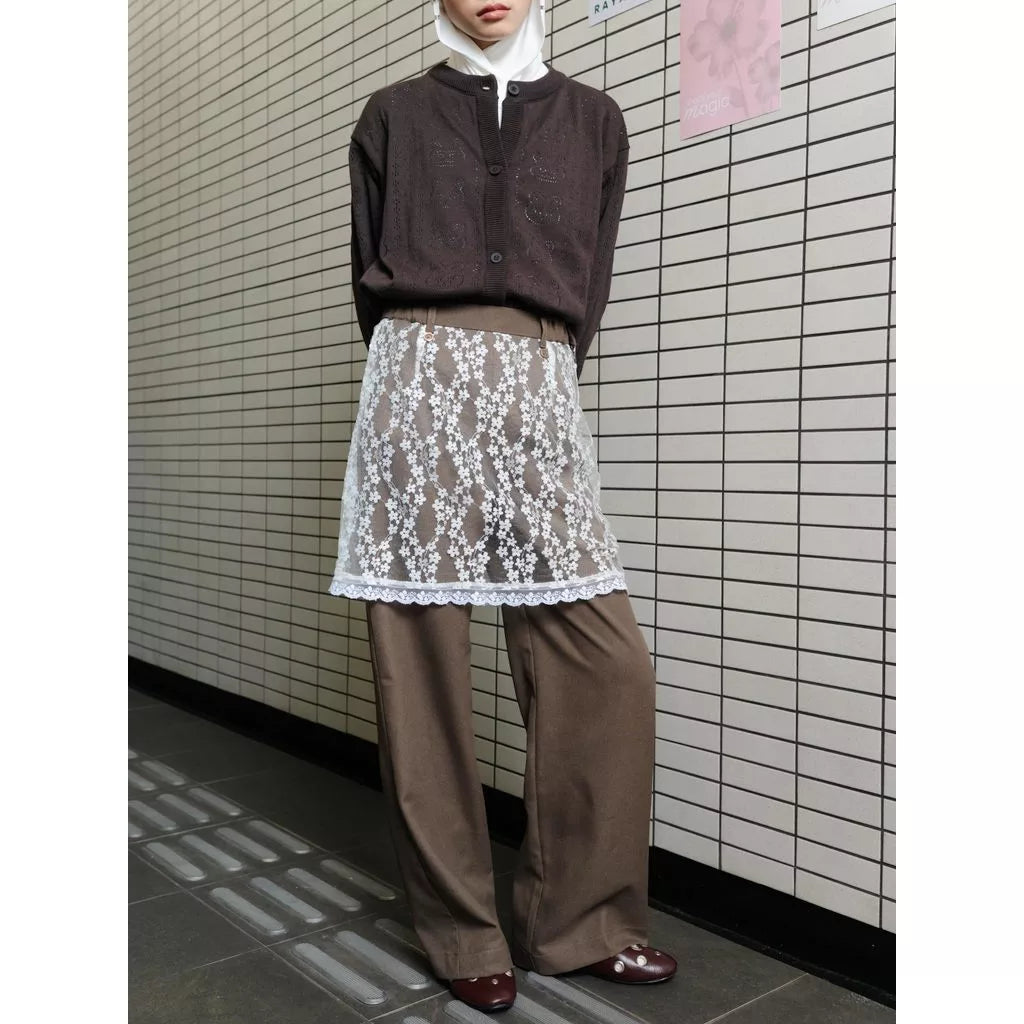 Person wearing a brown sweater and brown pants by Tome Ame with lace accents against a tiled wall.