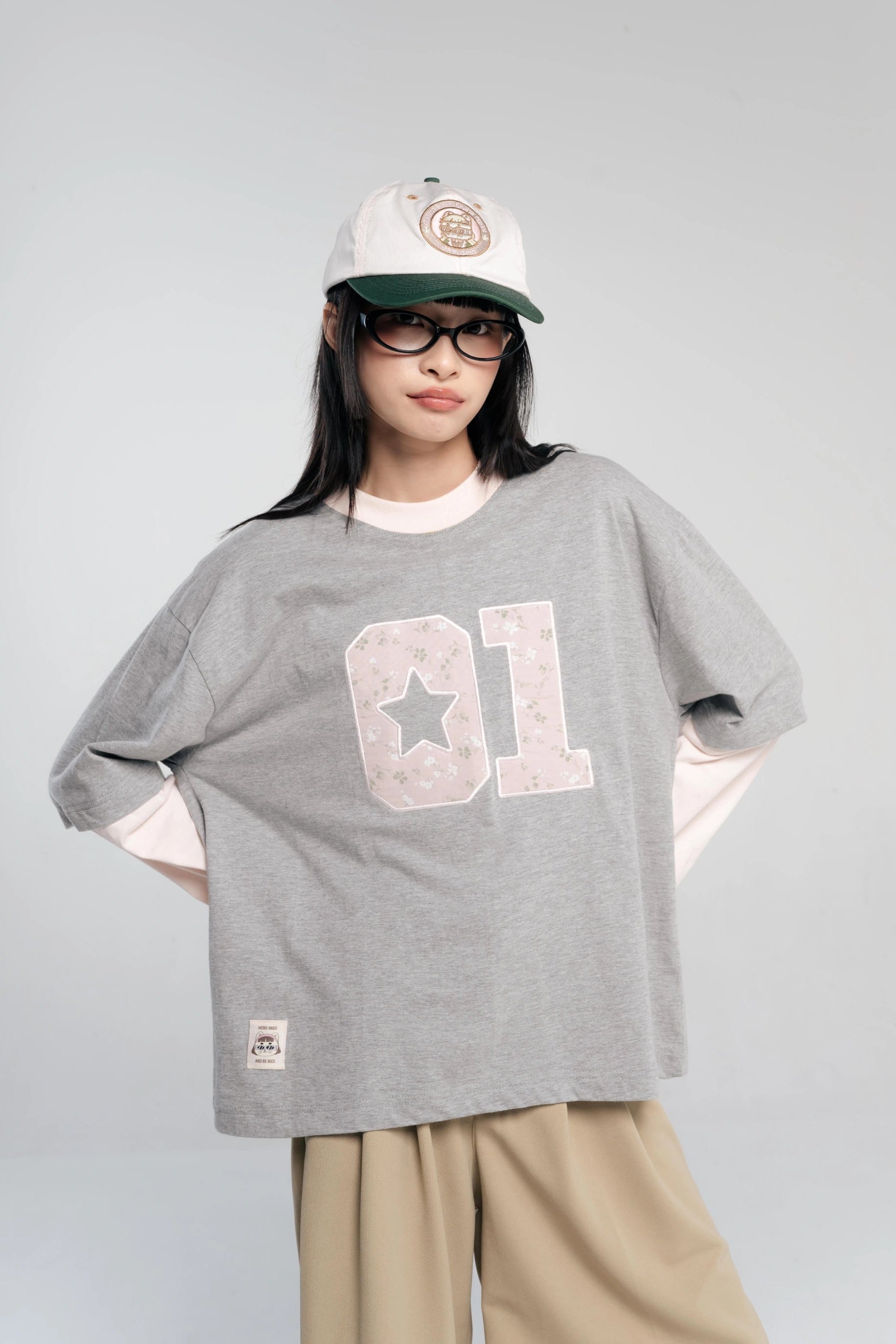 Person wearing a gray oversized t-shirt with a design by Tome Ame, beige pants, and a cap on a plain background