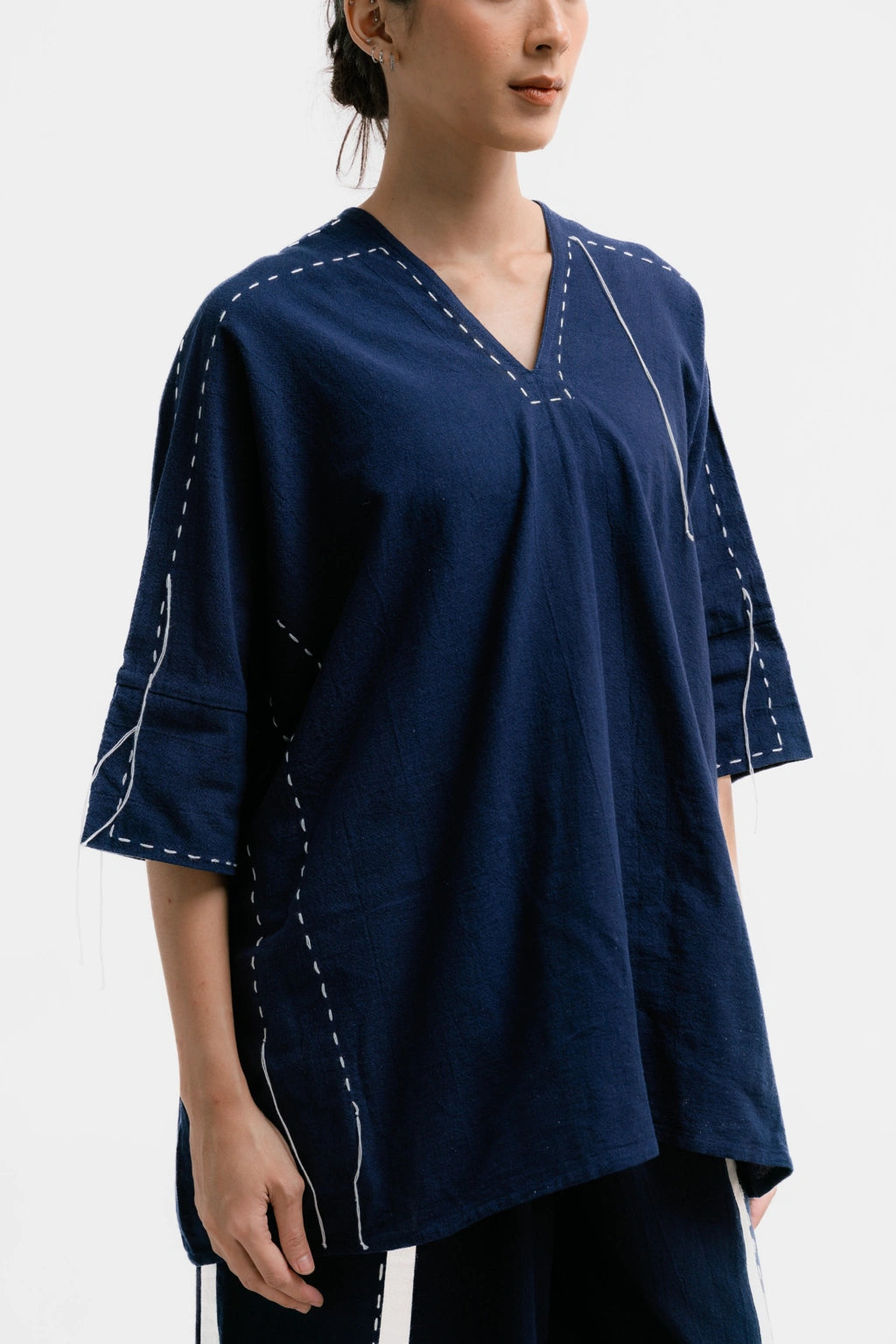 Woman wearing a navy blue blouse with white stitching from Damakara on a white background