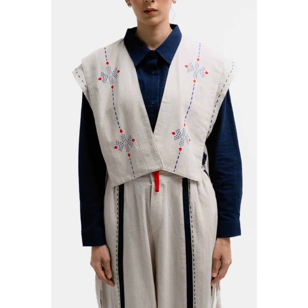 Person wearing a cream embroidered vest by Damakara over a navy shirt and pants on a white background