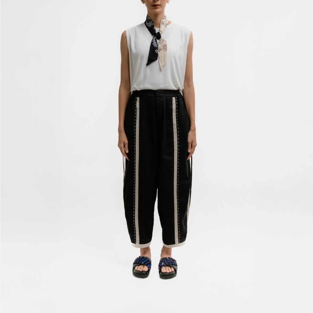 Person wearing a sleeveless top and black pants by Damakara with white trim on a white background