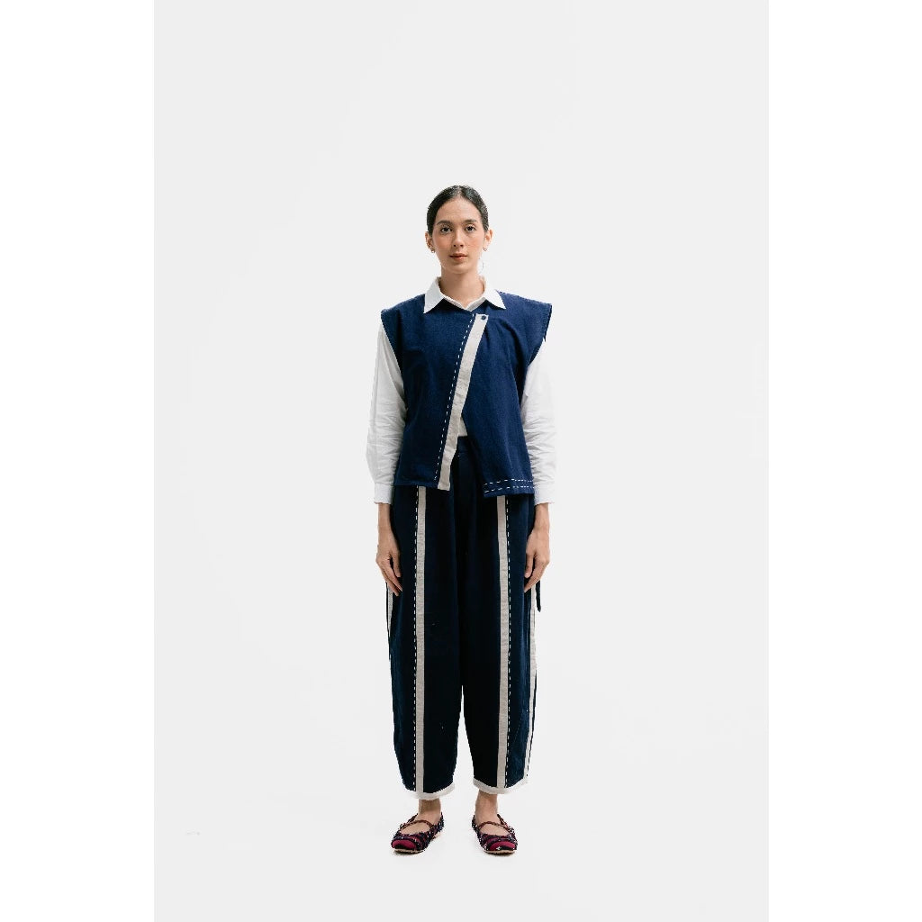 Person wearing a blue vest by Damakara over a white shirt with dark pants on a white background