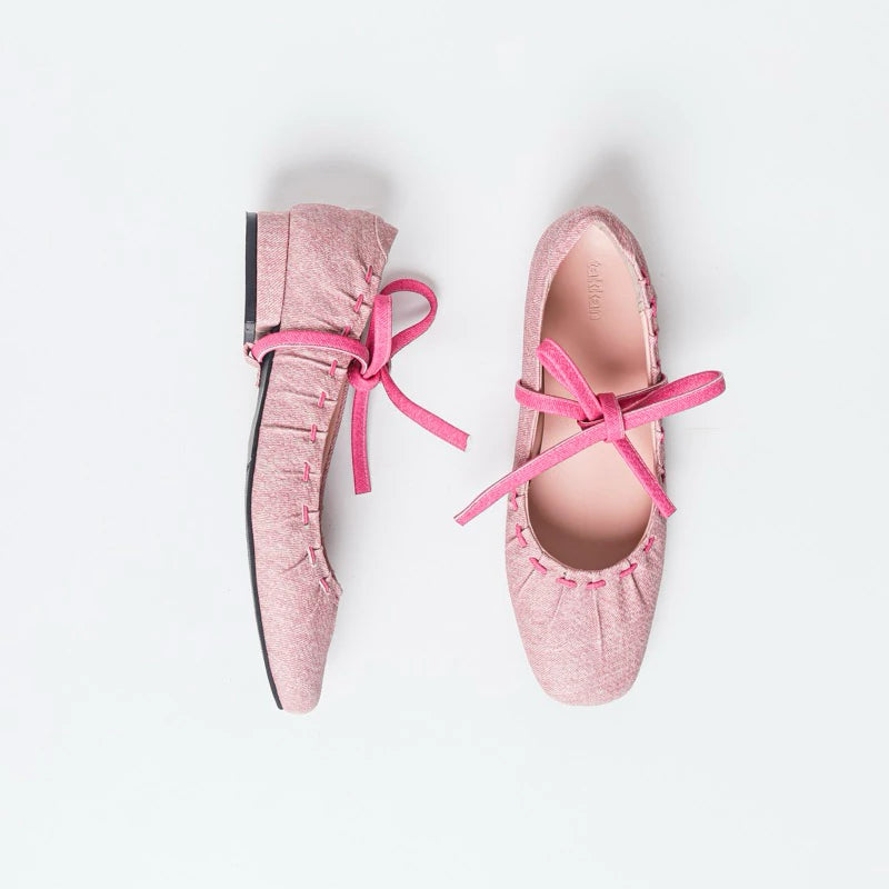 Pink flat shoes by Takkan with pink laces on a white background