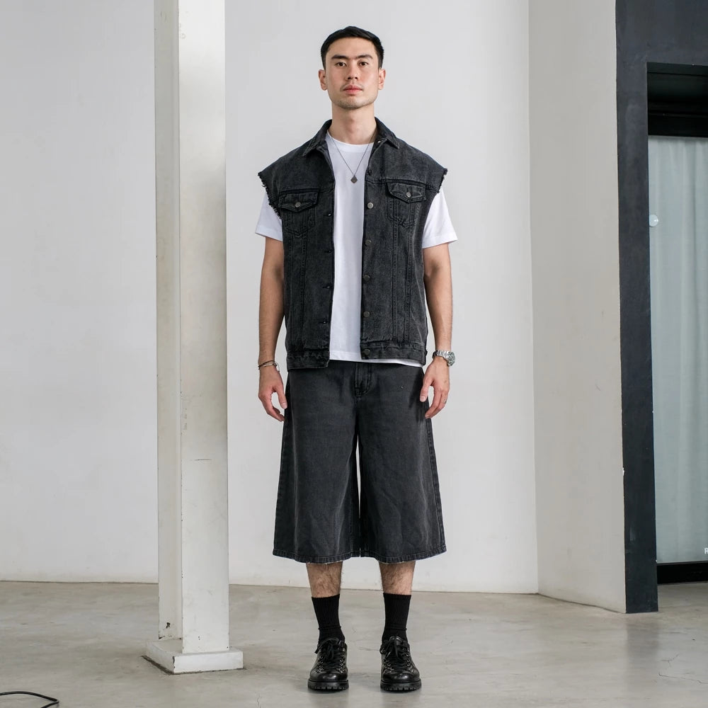 Man wearing a black vest, white t-shirt, and black jorts pants in an indoor setting.