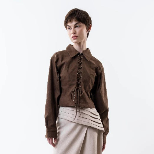 Person wearing a brown jacket by Morningsol with lace-up front and beige skirt on a white background