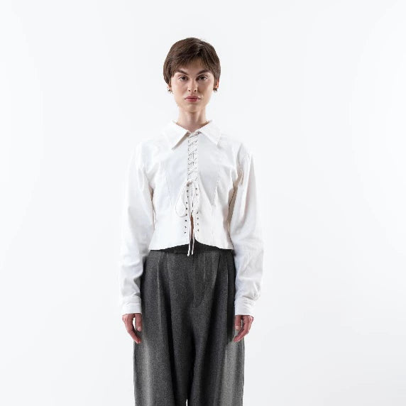 Person wearing a white jacket by Morningsol with lace details and gray pants on a white background