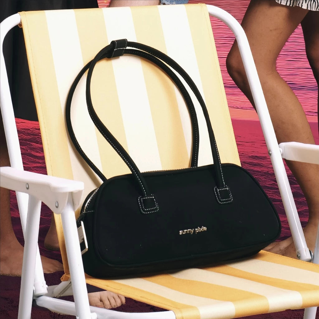 A person holding a black Juju Bag by Sunny Pixie with silver metallic hardware, the bag has a sleek, futuristic design with two handles.

Seorang wanita memegang tas wanita Juju berwarna hitam dari Sunny Pixie dengan aksesori logam perak, tas tersebut memiliki desain yang ramping dan futuristik dengan dua pegangan.