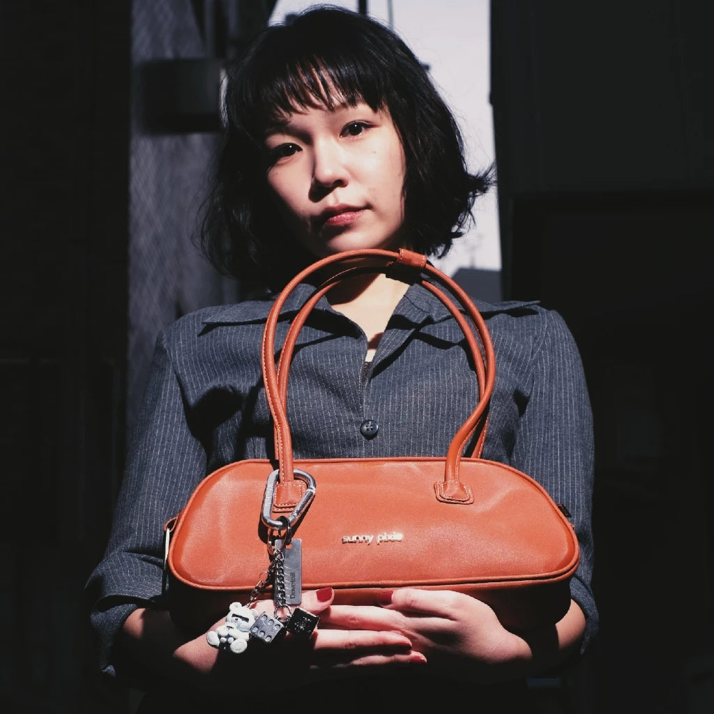 A person holding a brown Juju Bag by Sunny Pixie with silver metallic hardware, the bag has a sleek, futuristic design with two handles.

Seorang wanita memegang tas wanita Juju berwarna cokelat dari Sunny Pixie dengan aksesori logam perak, tas tersebut memiliki desain yang ramping dan futuristik dengan dua pegangan.