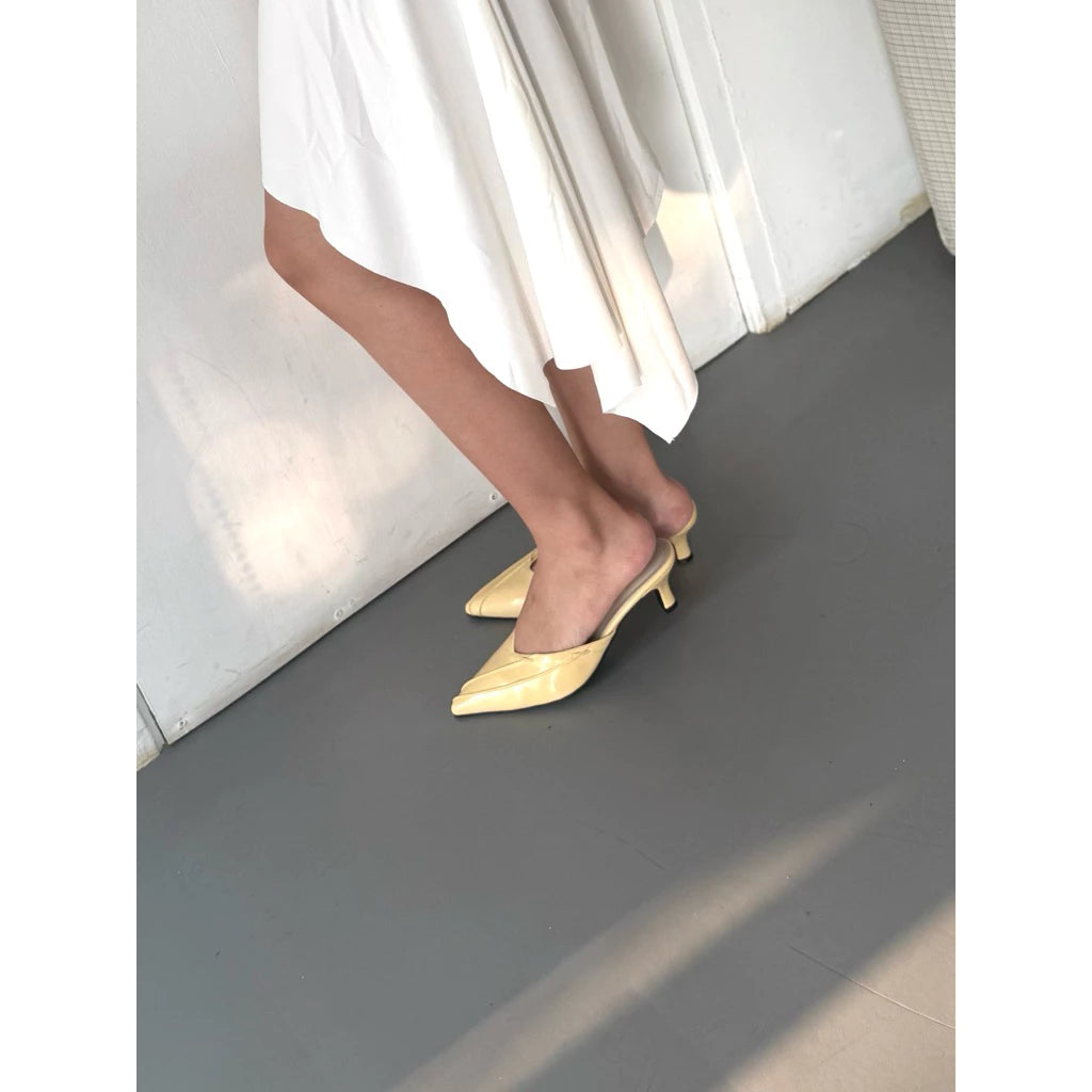 Person wearing light-colored high-heeled shoes by Takkan on a gray floor with white curtains in the background