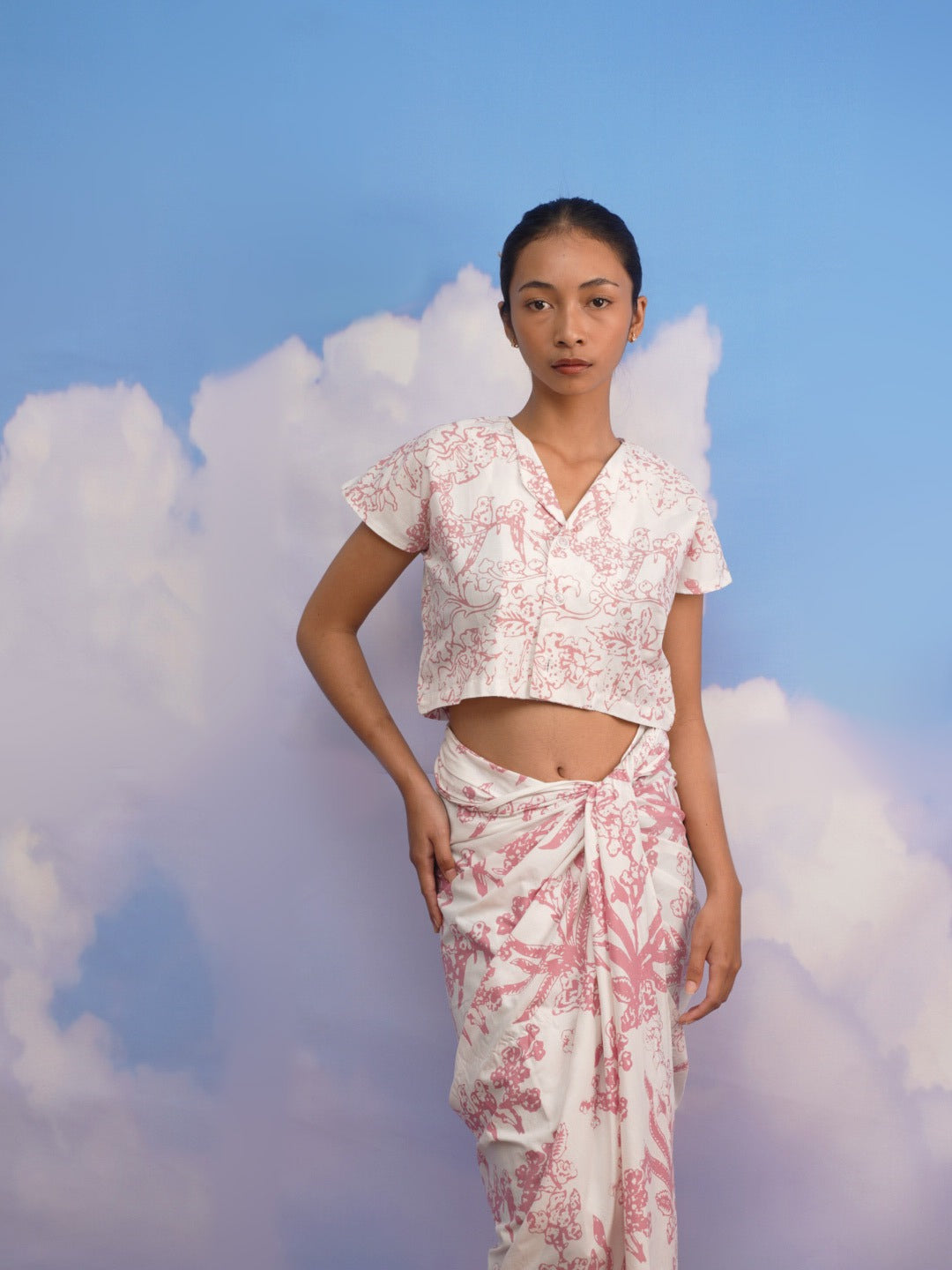 Woman wearing a pink floral outfit by Manikan against a blue sky with clouds