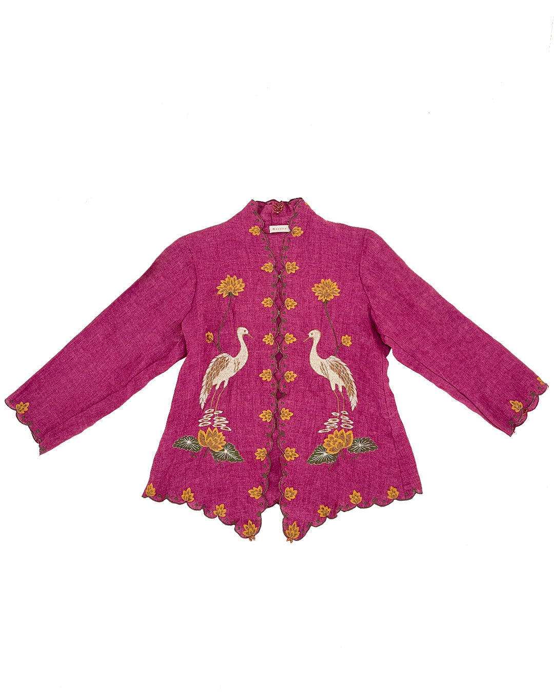 A magenta pink kebaya by Merona with long sleeves, a scalloped hem, and detailed embroidery of two white cranes, yellow flowers, and green leaves on the front, displayed flat against a white background.