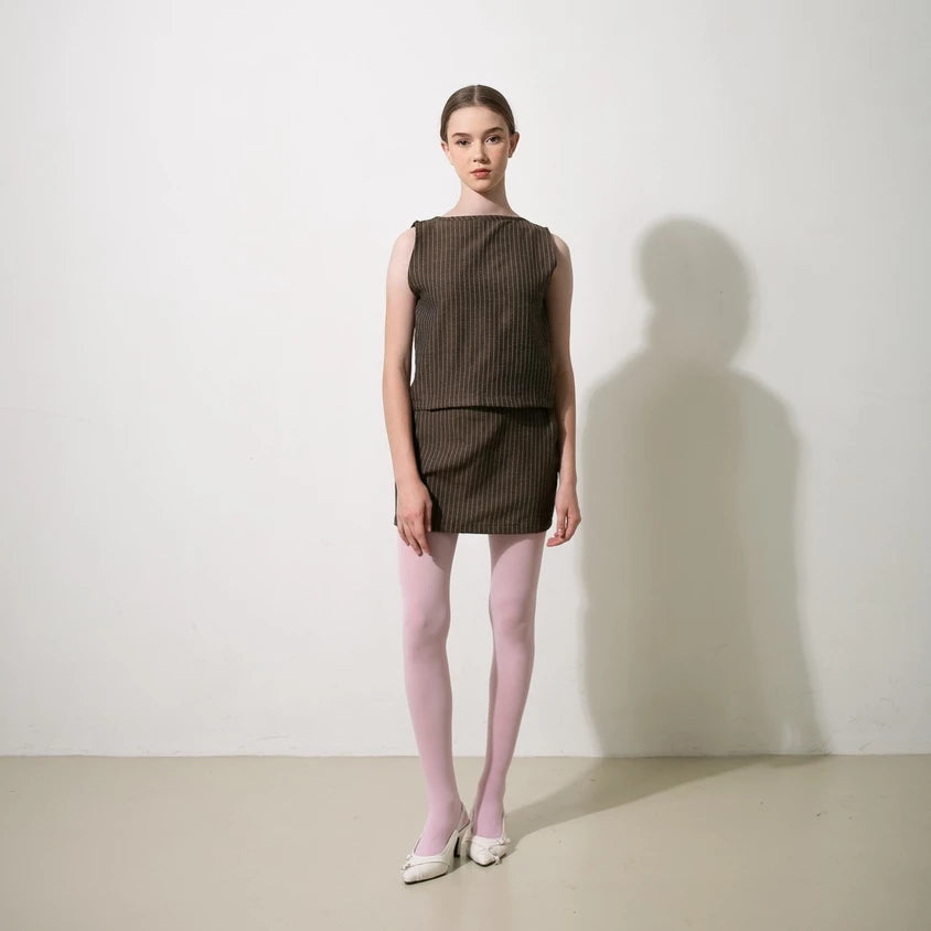 Model wearing a brown sleeveless top by Tuff Puff and skirt with pink tights against a white background