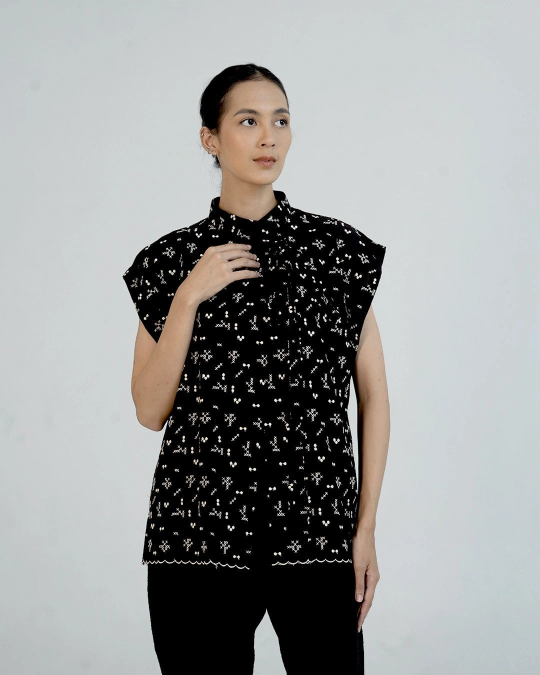 Woman wearing a black sleeveless outer by Damakara with white patterns on a plain background