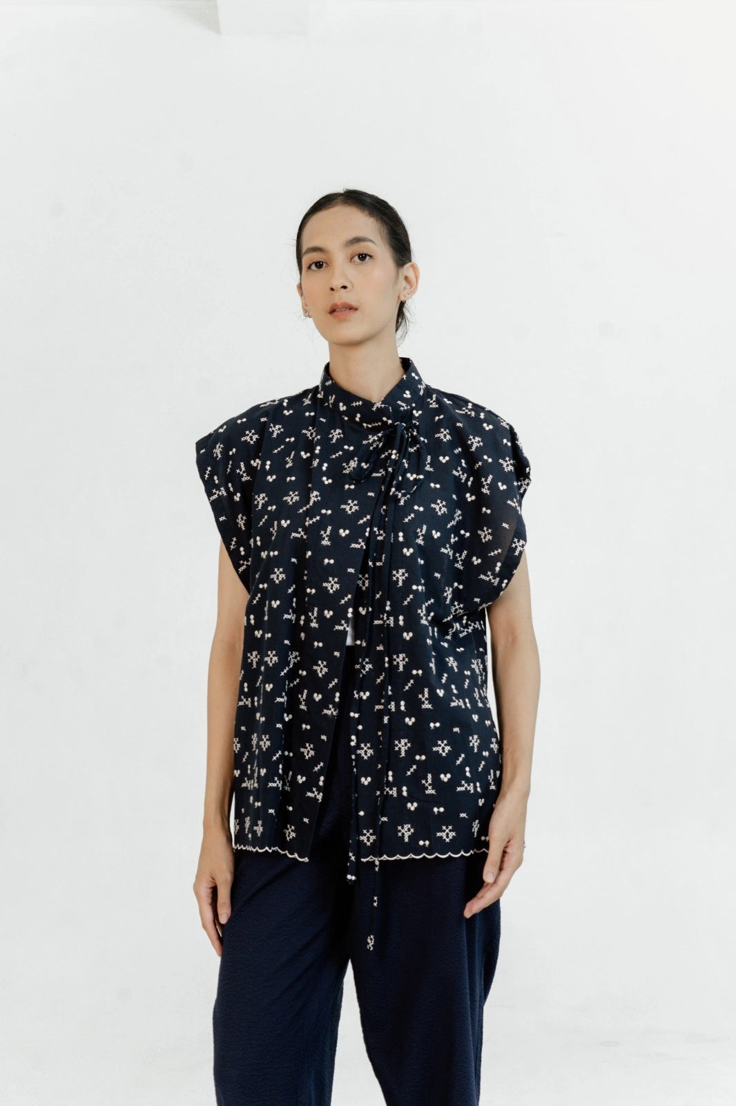 Person wearing a navy sleeveless outer by Damakara with white patterns on a white background