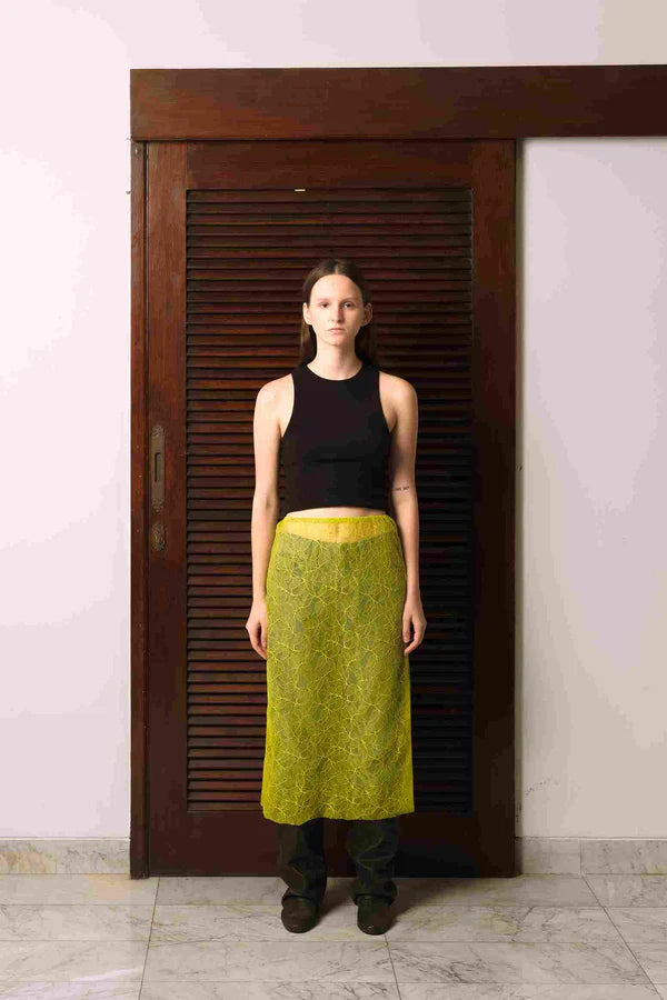 A person standing in a doorway wearing a midi length, straight cut lace skirt with an elastic waist and a black tank top.
