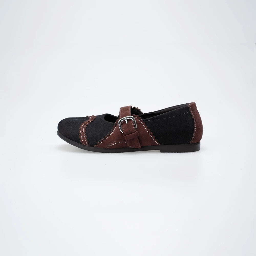 Black flat shoe with brown details, strap, and buckle on a white background