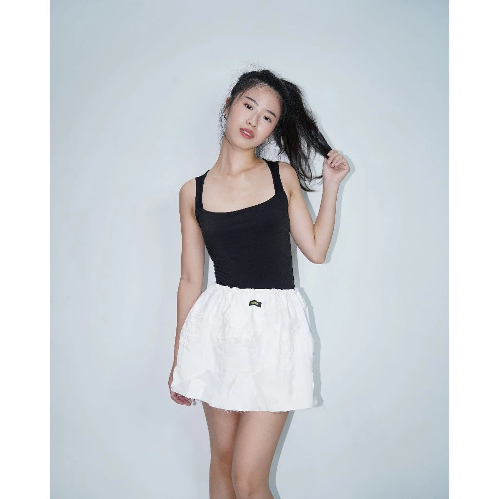 A woman wearing a black tank top and a white mini skirt with a puffy texture.