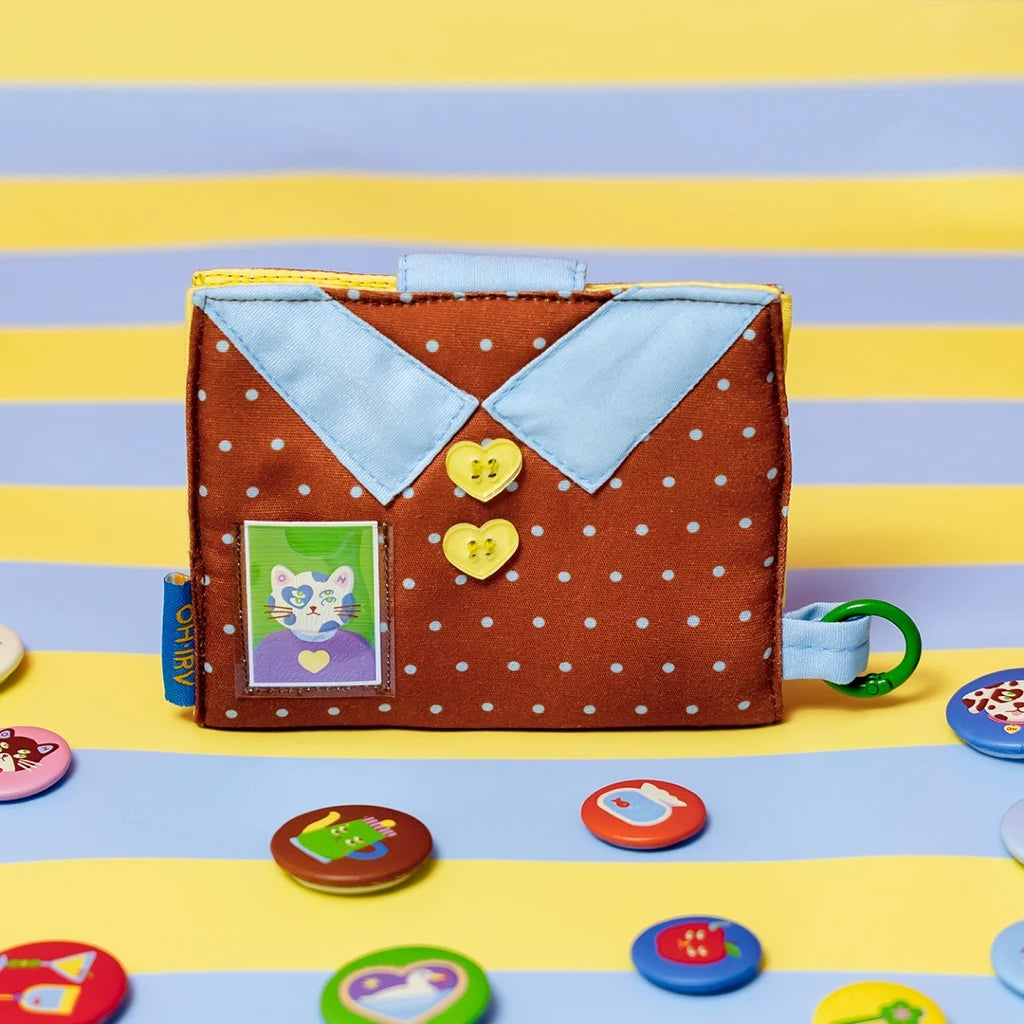 Wallet by Oh.Irv with a brown cover featuring a cat illustration, surrounded by colorful buttons on a striped background.