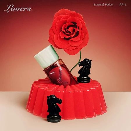 Perfume bottle from Kitschy on a red stand with a red rose and black horse figurines against a gradient background.