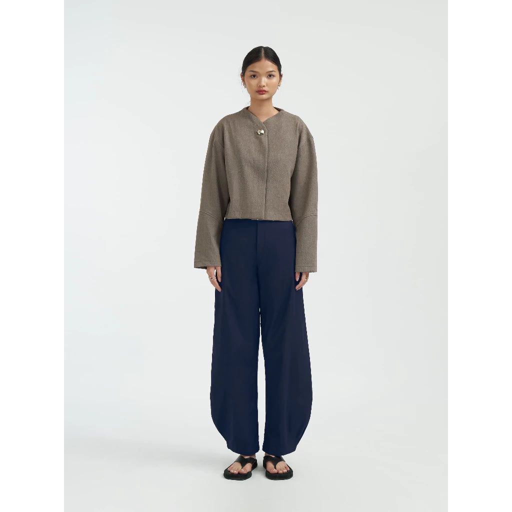 Woman wearing a brown jacket by Achete de Nous and navy pants on a white background