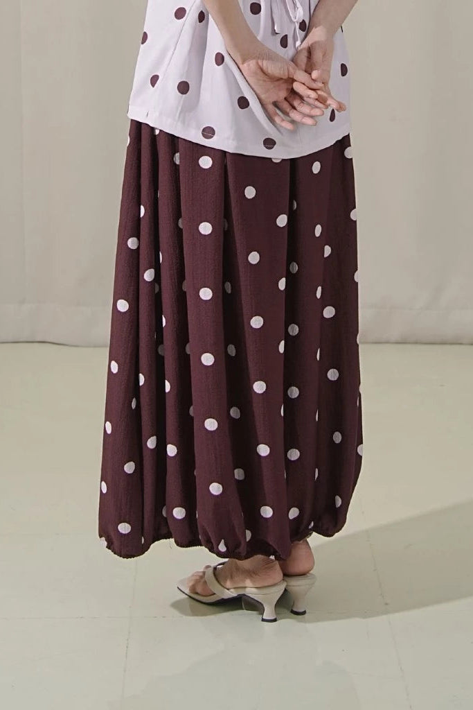 Person wearing a white top with red polka dots and a brown skirt with white polka dots by Tuff Puff on a plain background.