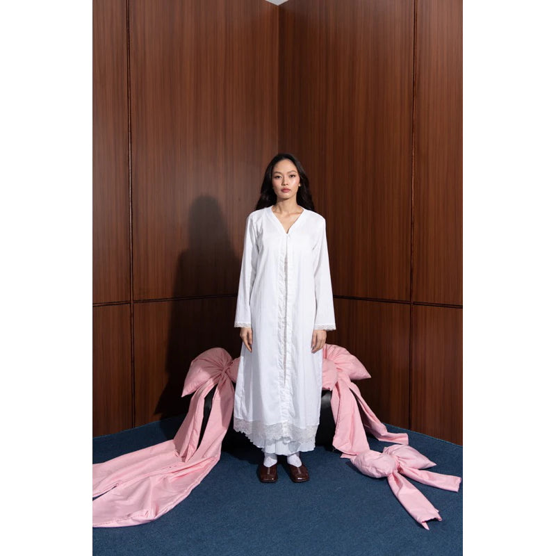 Woman in a white long outer by Tuff Puff standing between pink fabric in front of wooden panels