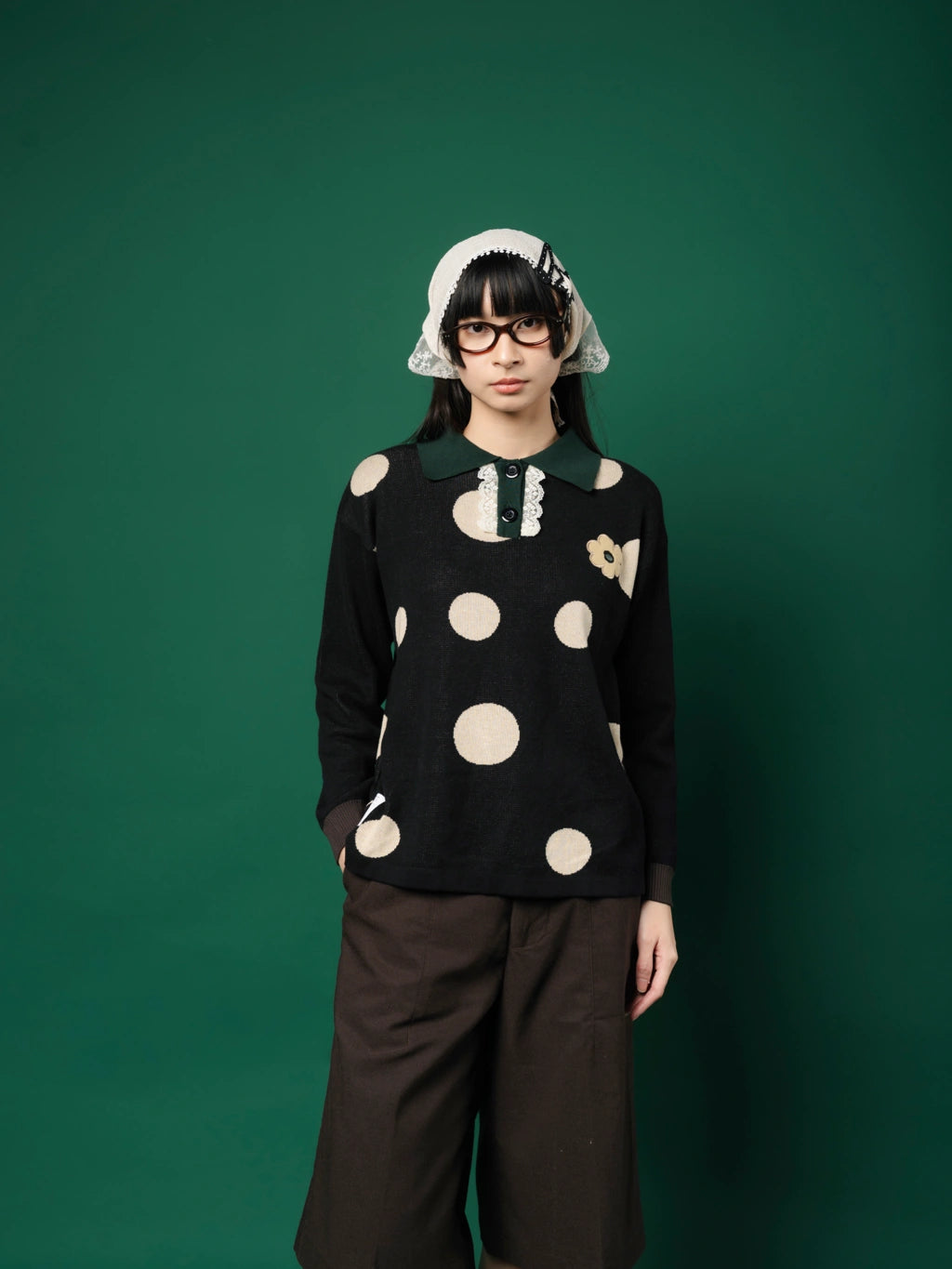 Person wearing a black sweater with white polka dots and a white headscarf against a green background