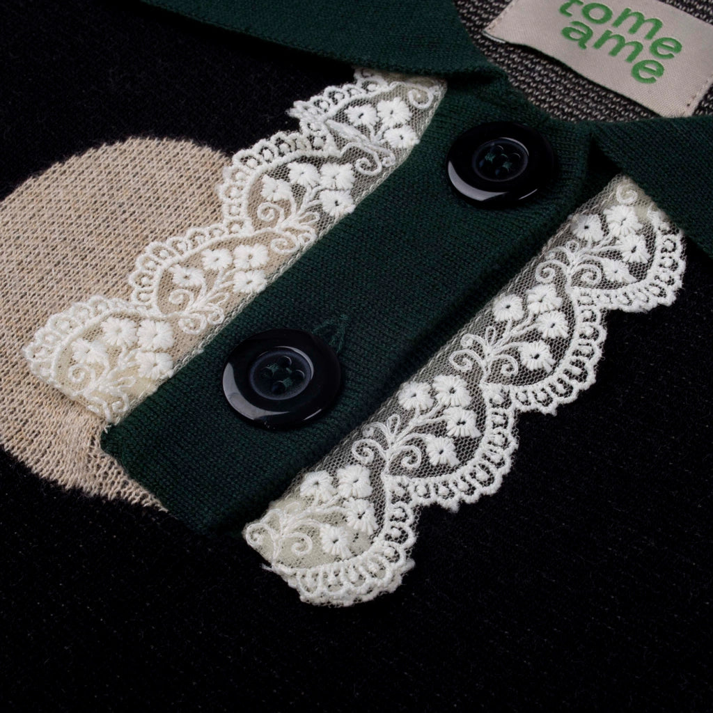 Close-up of a sweater with lace details and buttons on a dark background.
