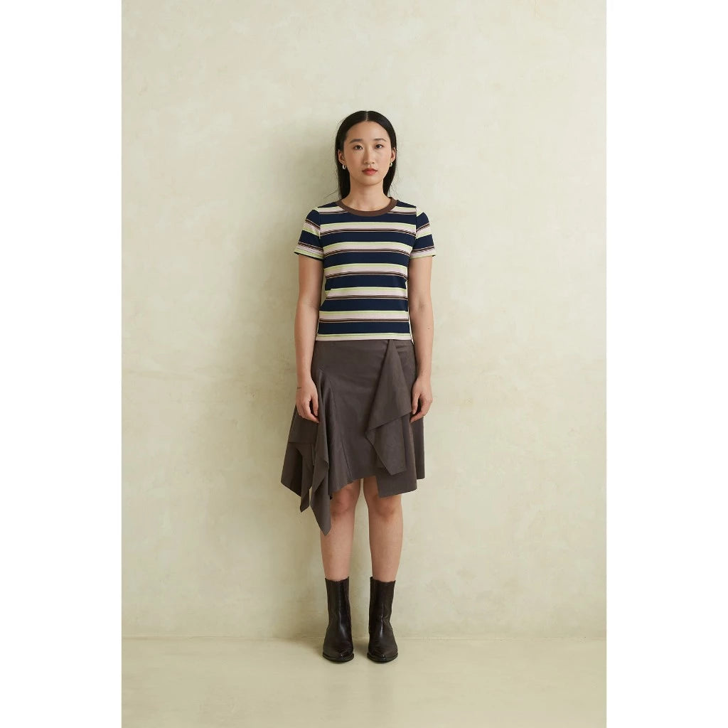 Woman wearing a striped shirt and grey ruffled skirt against a plain background