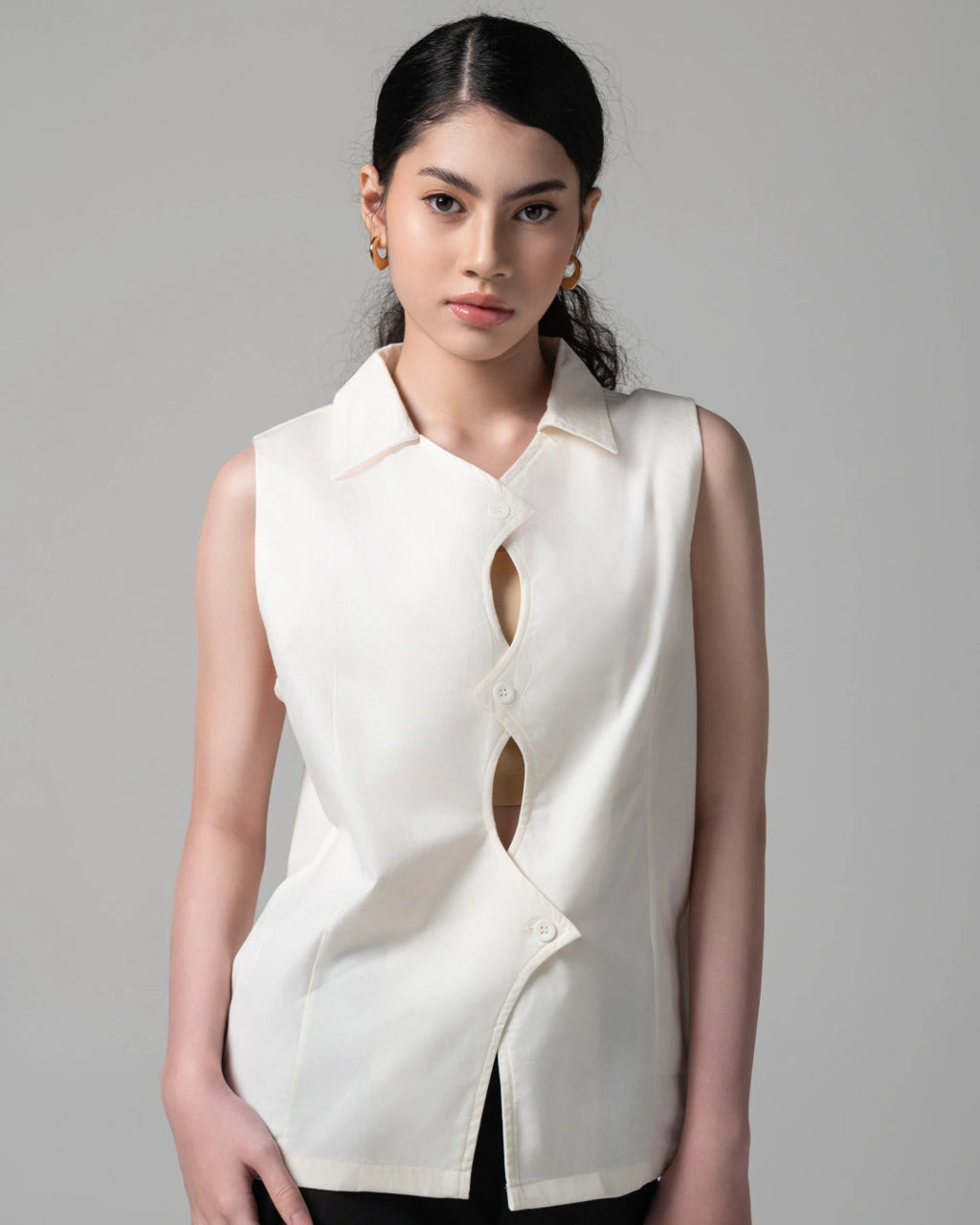 Woman wearing a white sleeveless blouse with cut-out design by Kajuaruna on a gray background