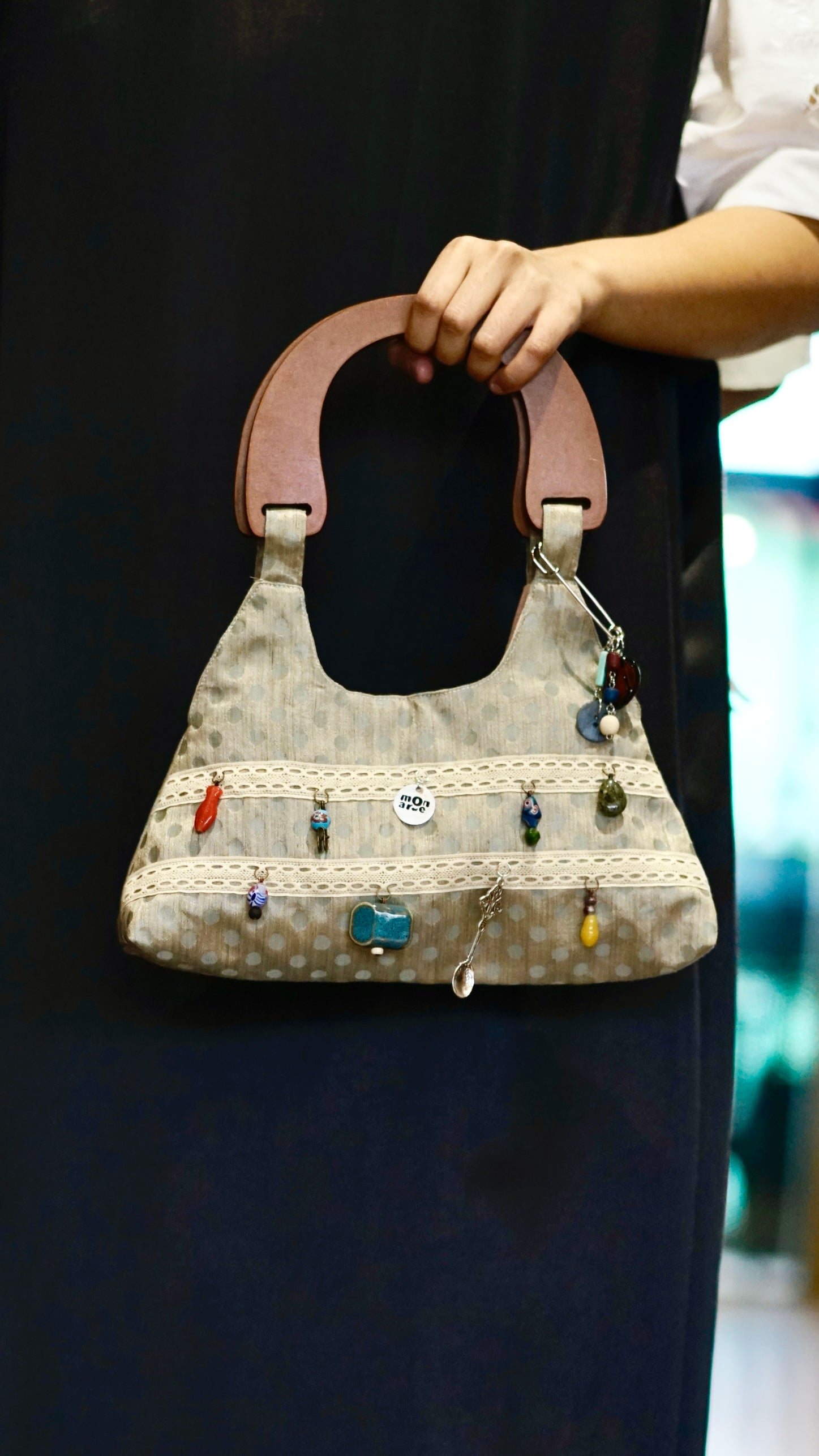 Women's trapezoid handbag with decorative charms held by a person against a dark background.

Tas tangan wanita berbentuk trapesium dengan hiasan manik-manik yang dipegang oleh seseorang di latar belakang gelap.