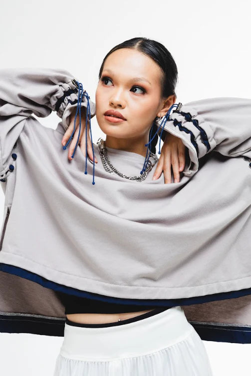 Woman wearing a light gray oversized sweater by Wad Studio with black and blue accents, posing against a white background