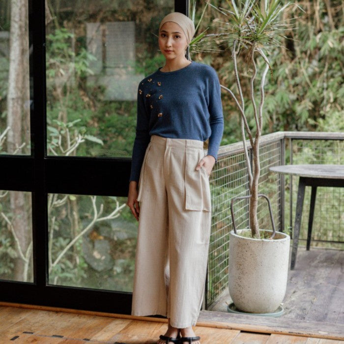 Person wearing a denim blue beaded sweater from Damakara and beige pants in a room with furniture.